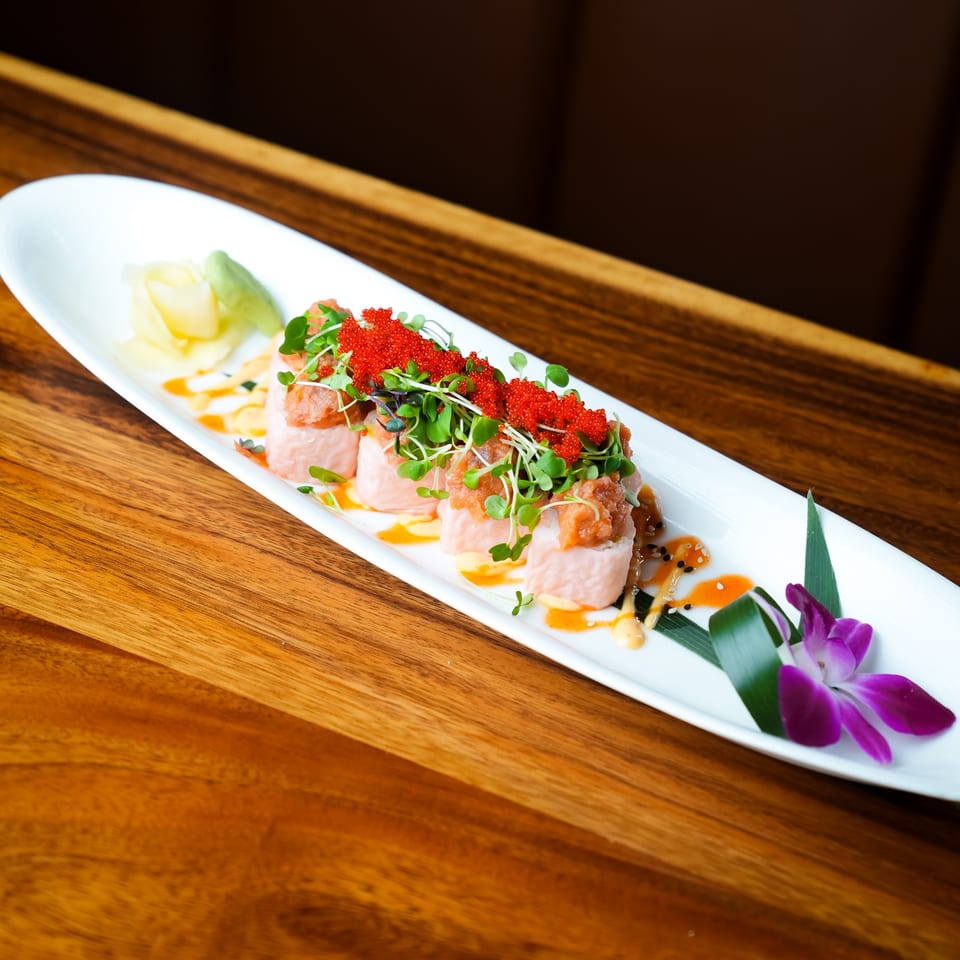 Koy Restaurant's sushi rolls topped with red roe, microgreens, and sauce, garnished with an orchid.