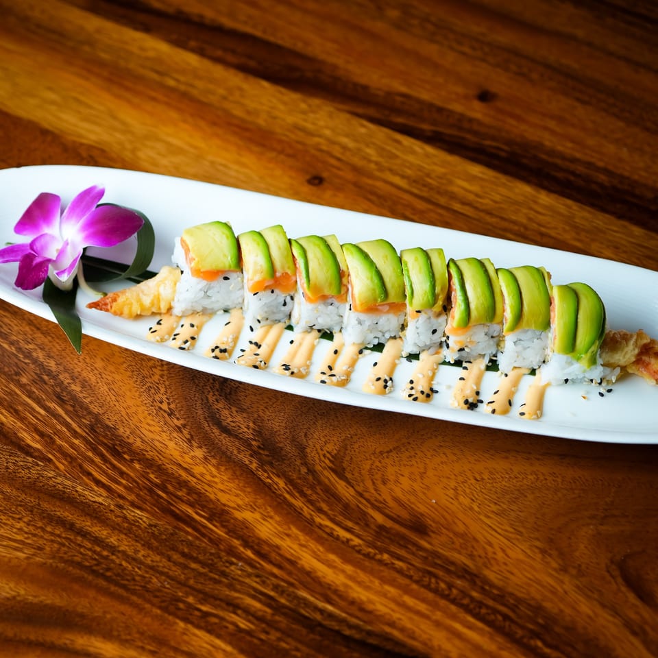 Dragon roll sushi with avocado, salmon, and tempura shrimp, garnished with a purple orchid.