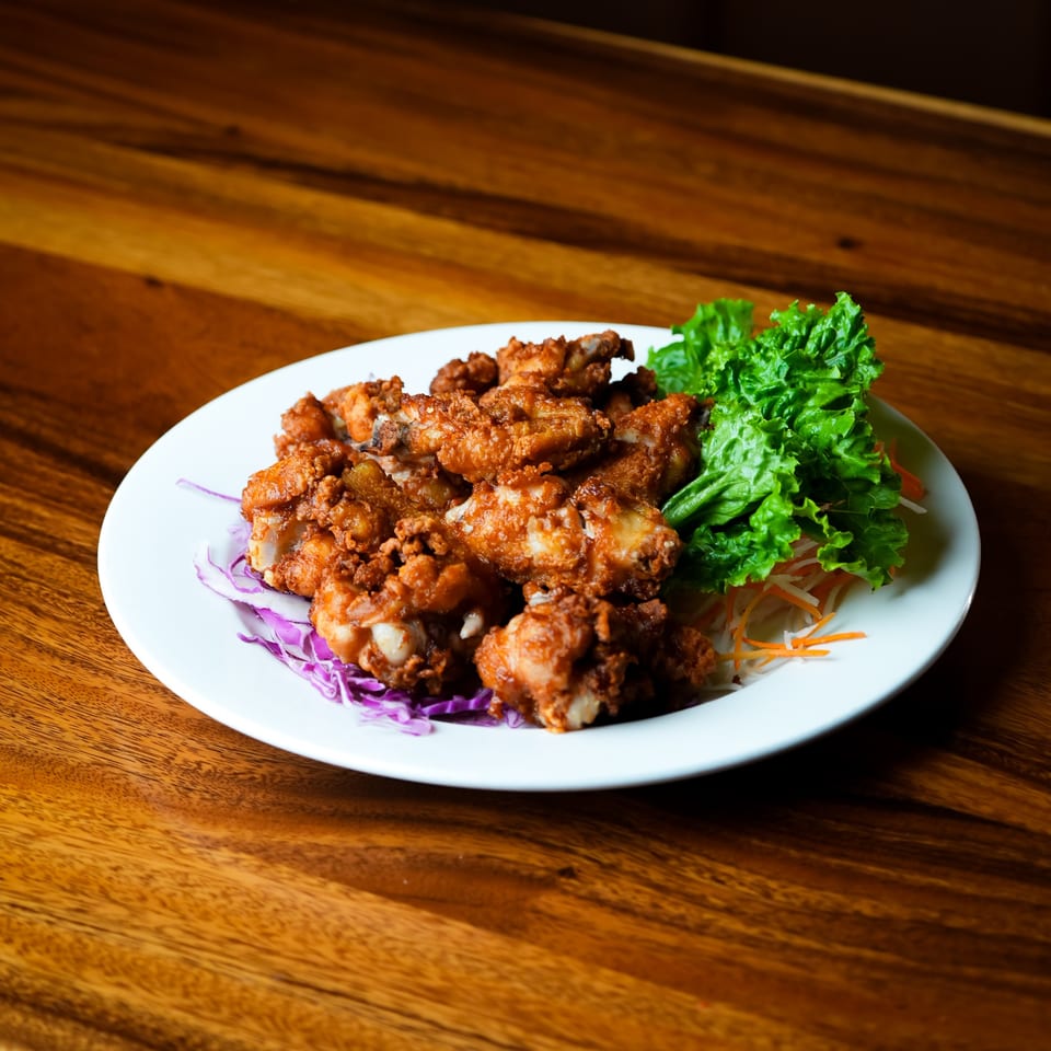 Crispy fried chicken pieces with lettuce, shredded carrots, and purple cabbage on a white plate.