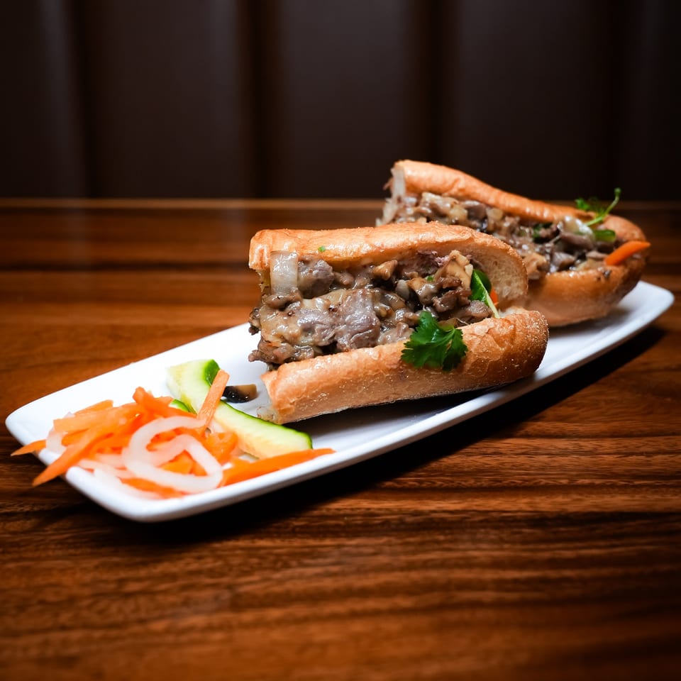 Two hearty sandwiches filled with meat and onions, served with pickled carrots and cucumbers.