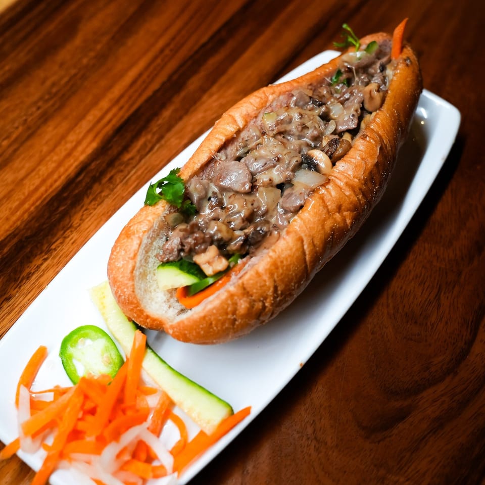 A banh mi sandwich filled with mushrooms and meat, served with pickled vegetables on a white plate.