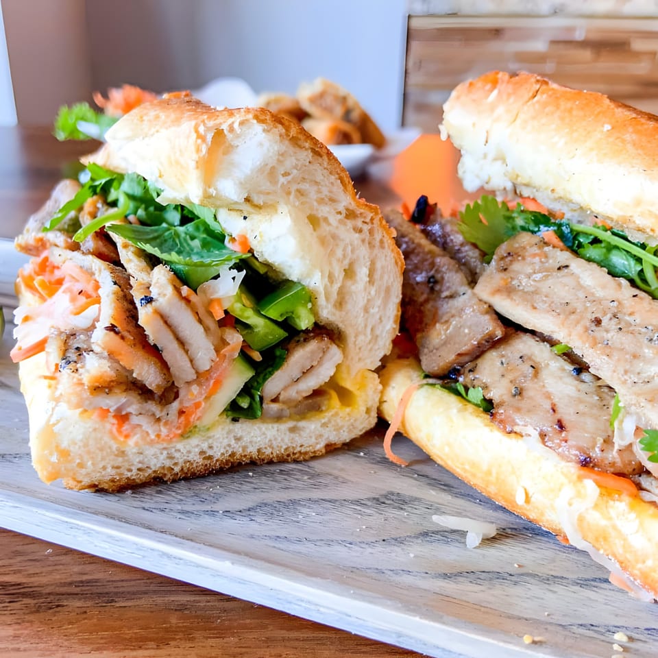 Two Koy Restaurant banh mi sandwiches filled with meat, fresh herbs, and pickled vegetables on a wooden board.